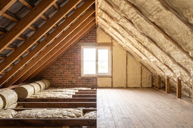 A loft split visually down the middle: on one side neat rolled mineral wool insulation between joists with clean bare rafters