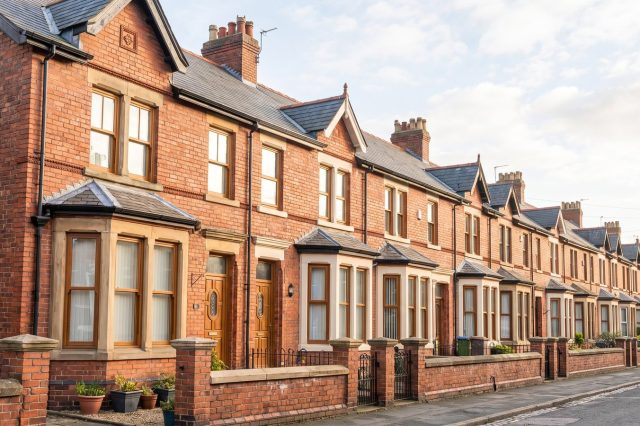 A row of red brick Victorian terraced houses in a northern English city on a bright sunny morning, bay windows, low front walls