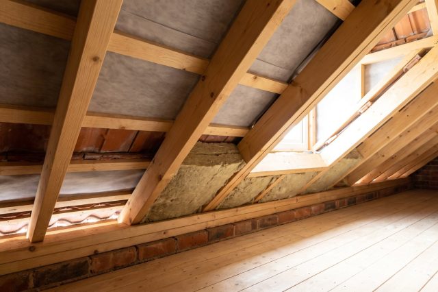 A British loft eaves detail in bright daylight showing the ventilation gap at the wall plate, clean timber rafters