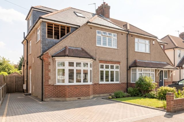 A classic British suburban semi-detached house with a pebbledash and brick facade, bay window and neat driveway, under bright soft sunshine