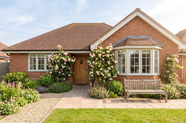 An older British couple's home exterior in gentle warm sunshine, a well-kept bungalow with a mature front garden
