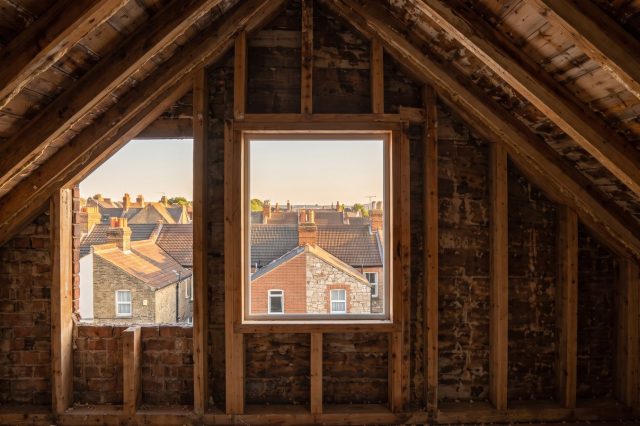 A wide sunny view over British rooftops towards a clear open horizon at golden hour brightness, chimney stacks and tiled roofs receding