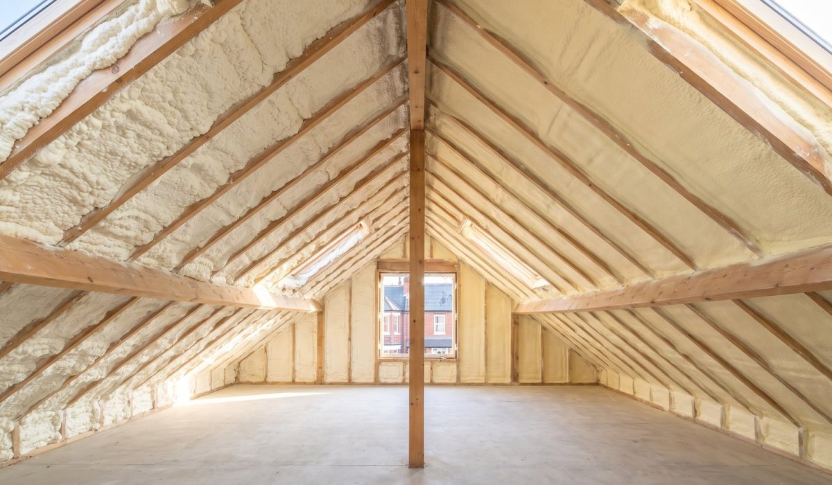 A British loft roof slope divided down the middle: one half coated in soft spongy off-white open-cell foam