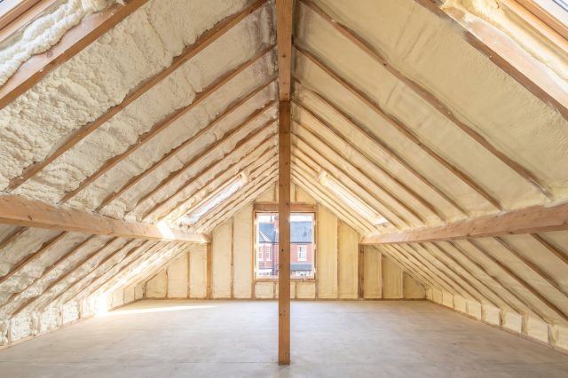 A British loft roof slope divided down the middle: one half coated in soft spongy off-white open-cell foam